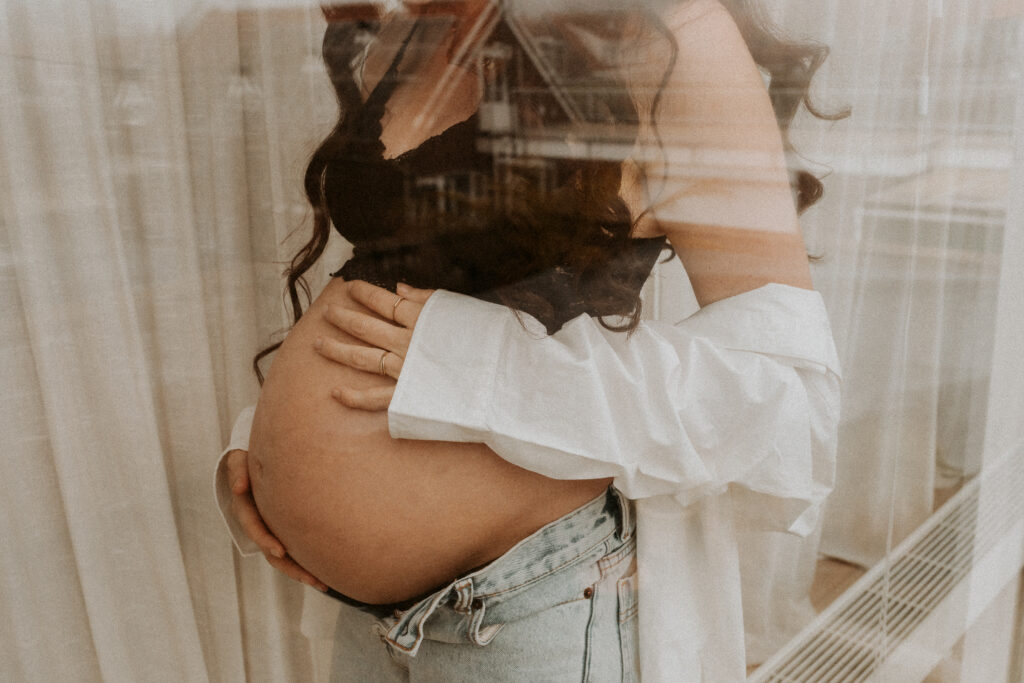 Kleur foto van een zwangere vrouw bij het raam in haar huis in Zeeland. 
